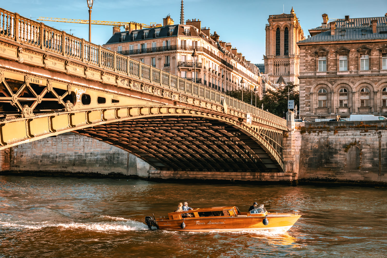 A small varnished boat passing beneath an ornate city bridge.