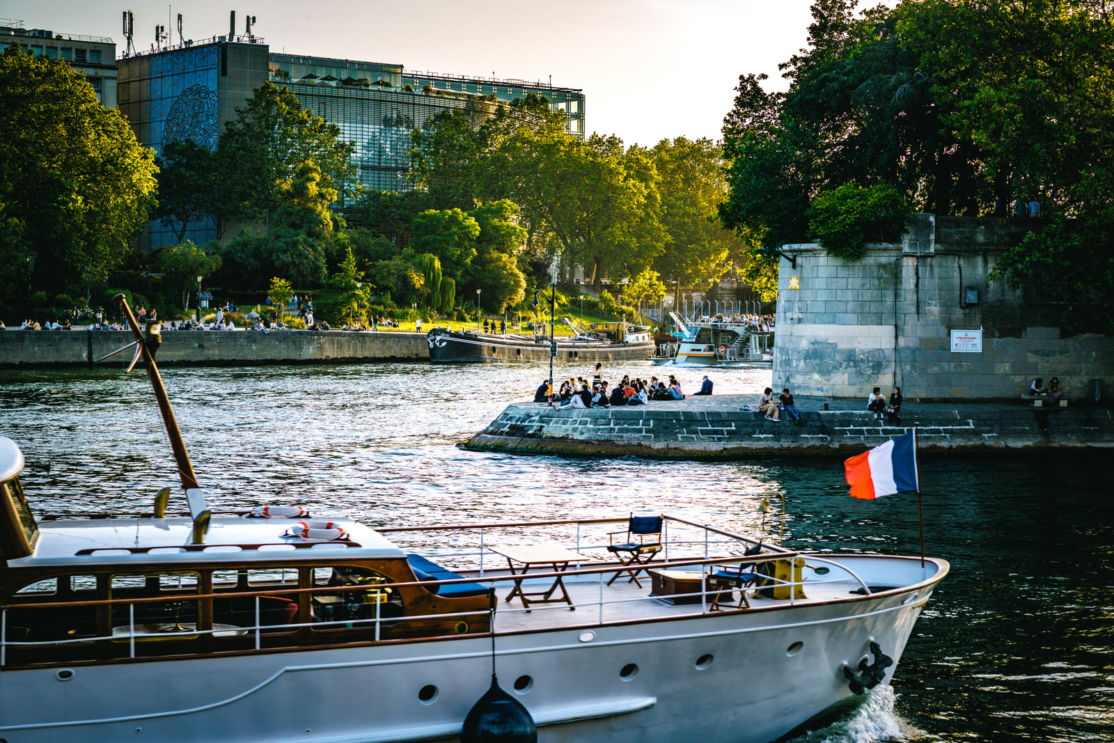 A wooden boat cruising past dense green trees on the river.