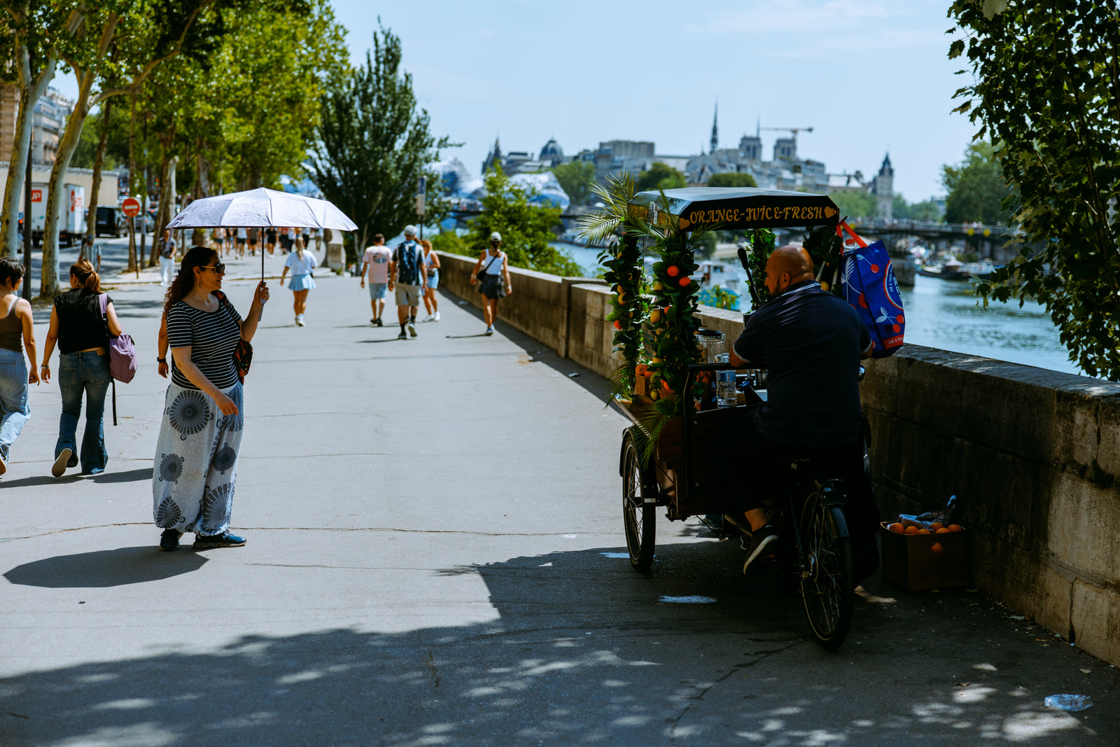 People strolling along a shaded riverside promenade.