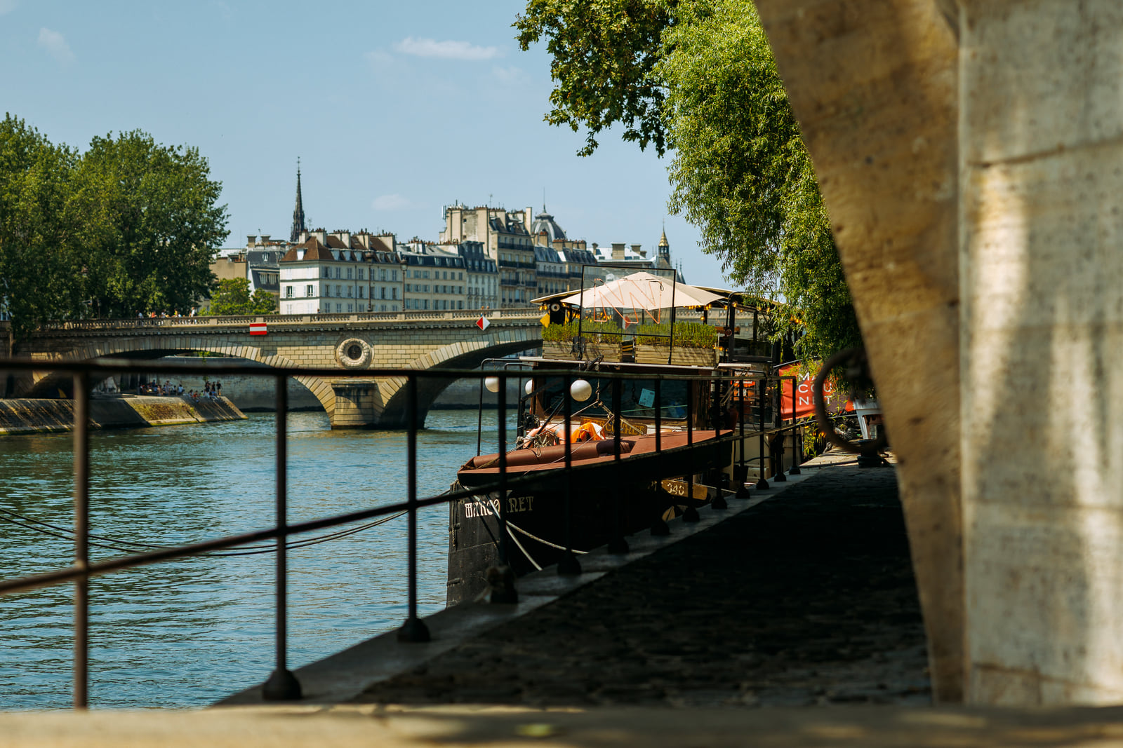 Riverboats and bridges layered through a gap in the embankment.