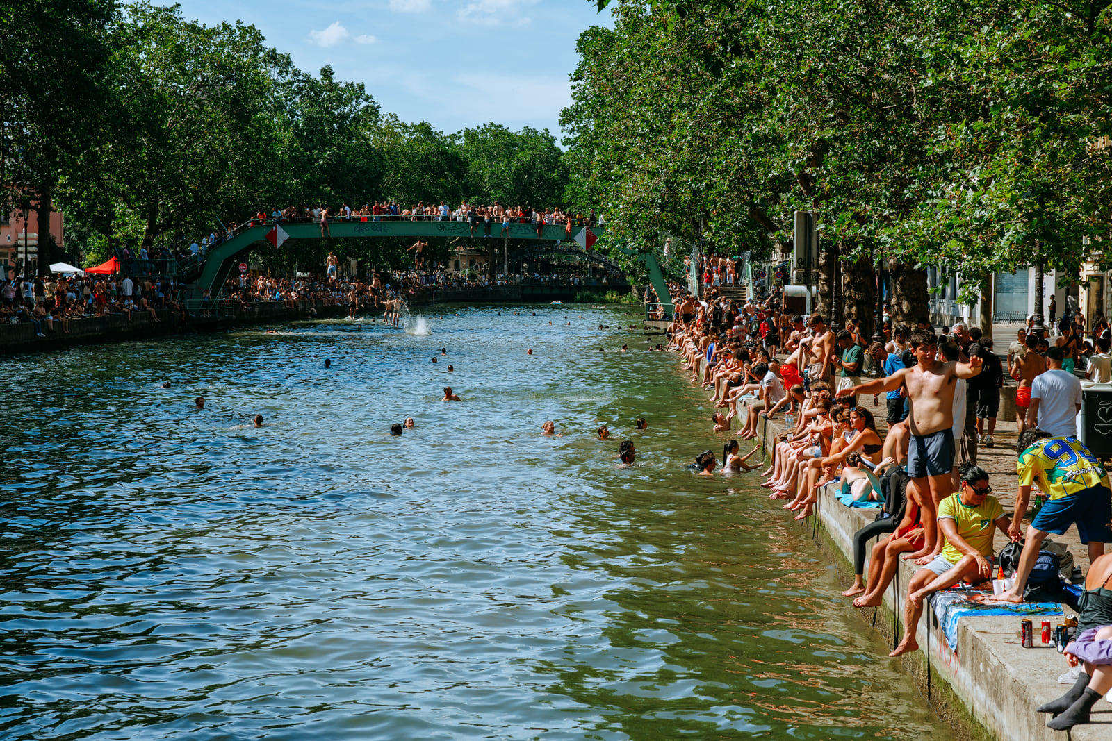 A wide view along a canal crowded with people in summer.
