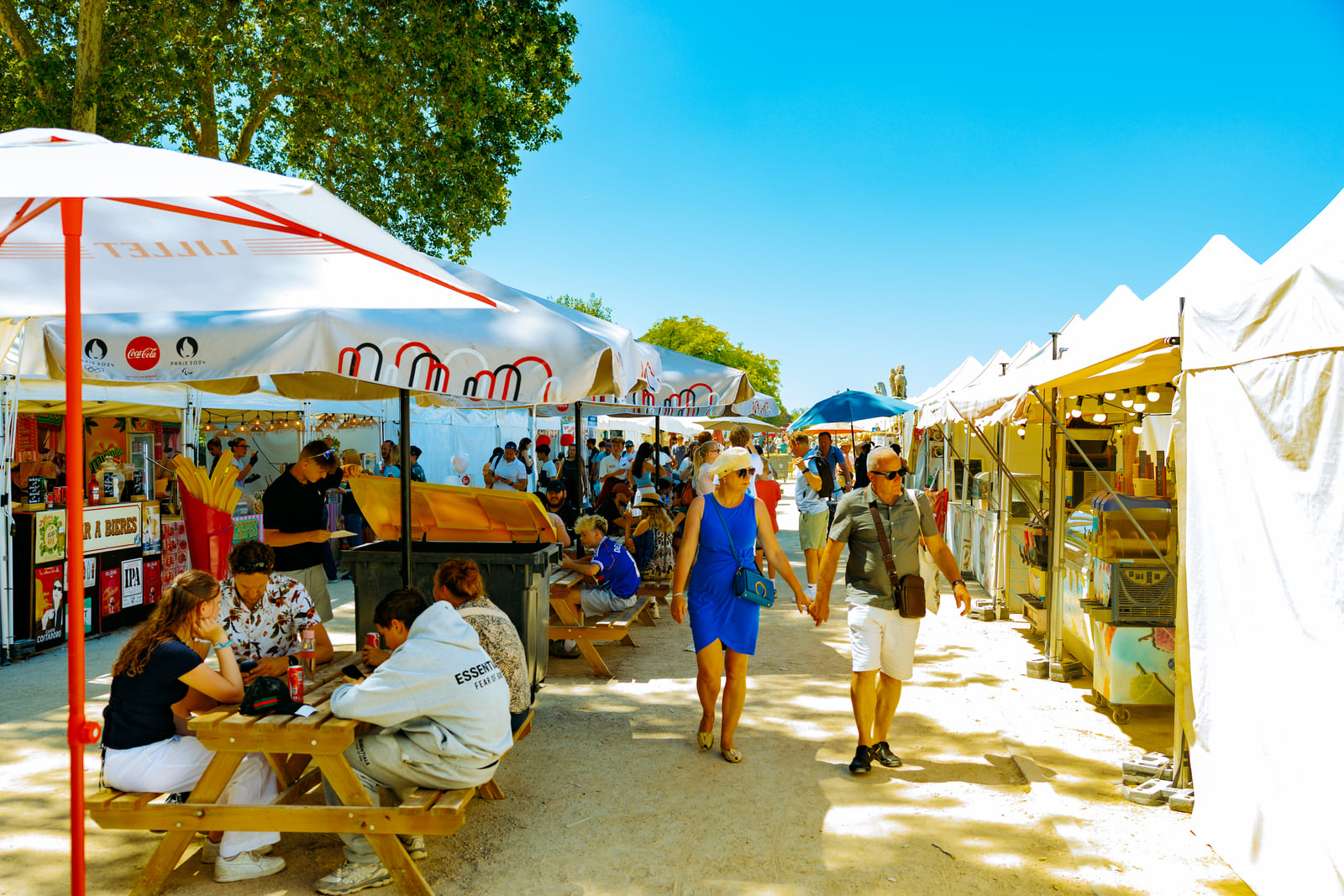 A bright open-air market stretching beneath trees and parasols.