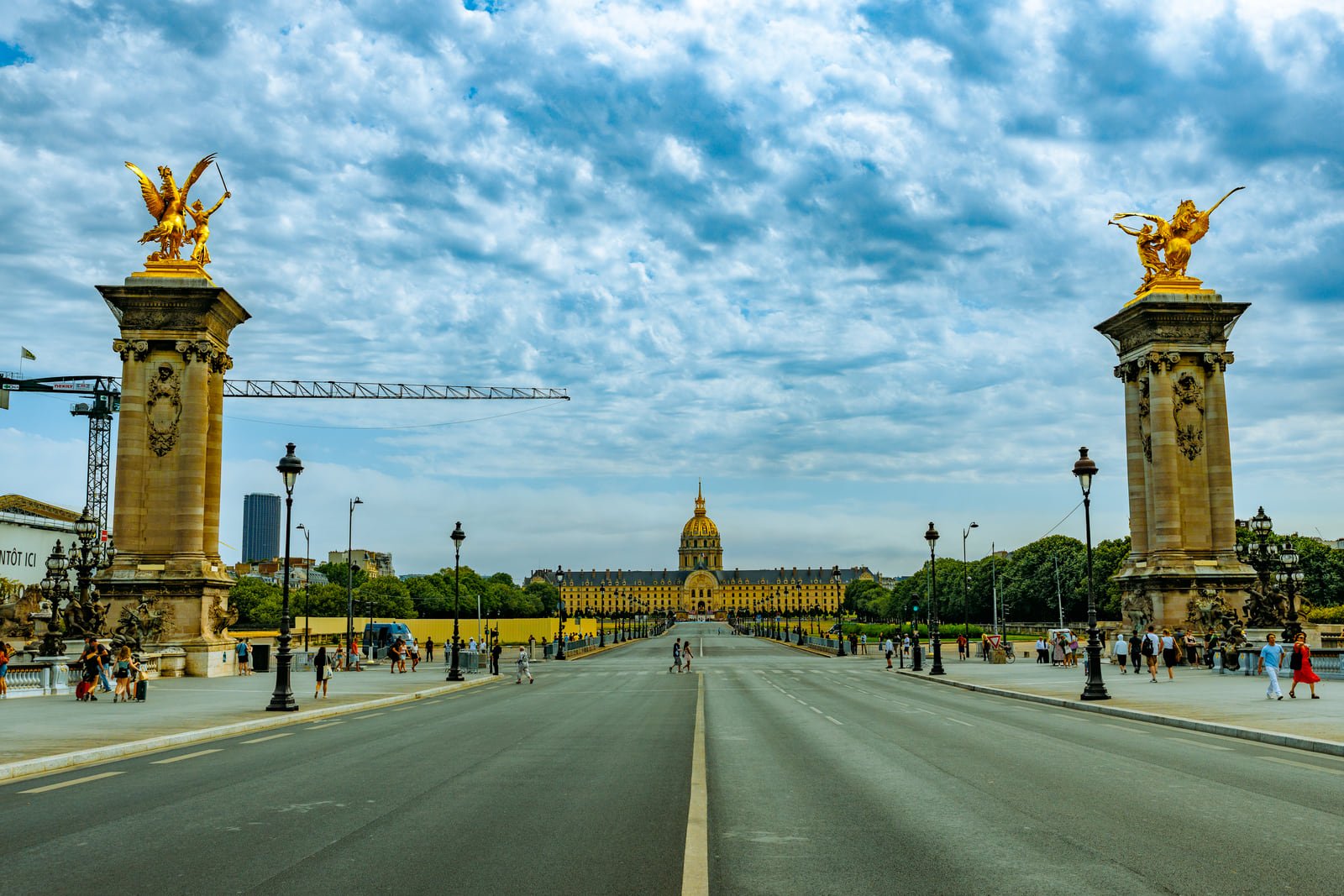 An open avenue framed by gilded statues beneath a textured blue sky.