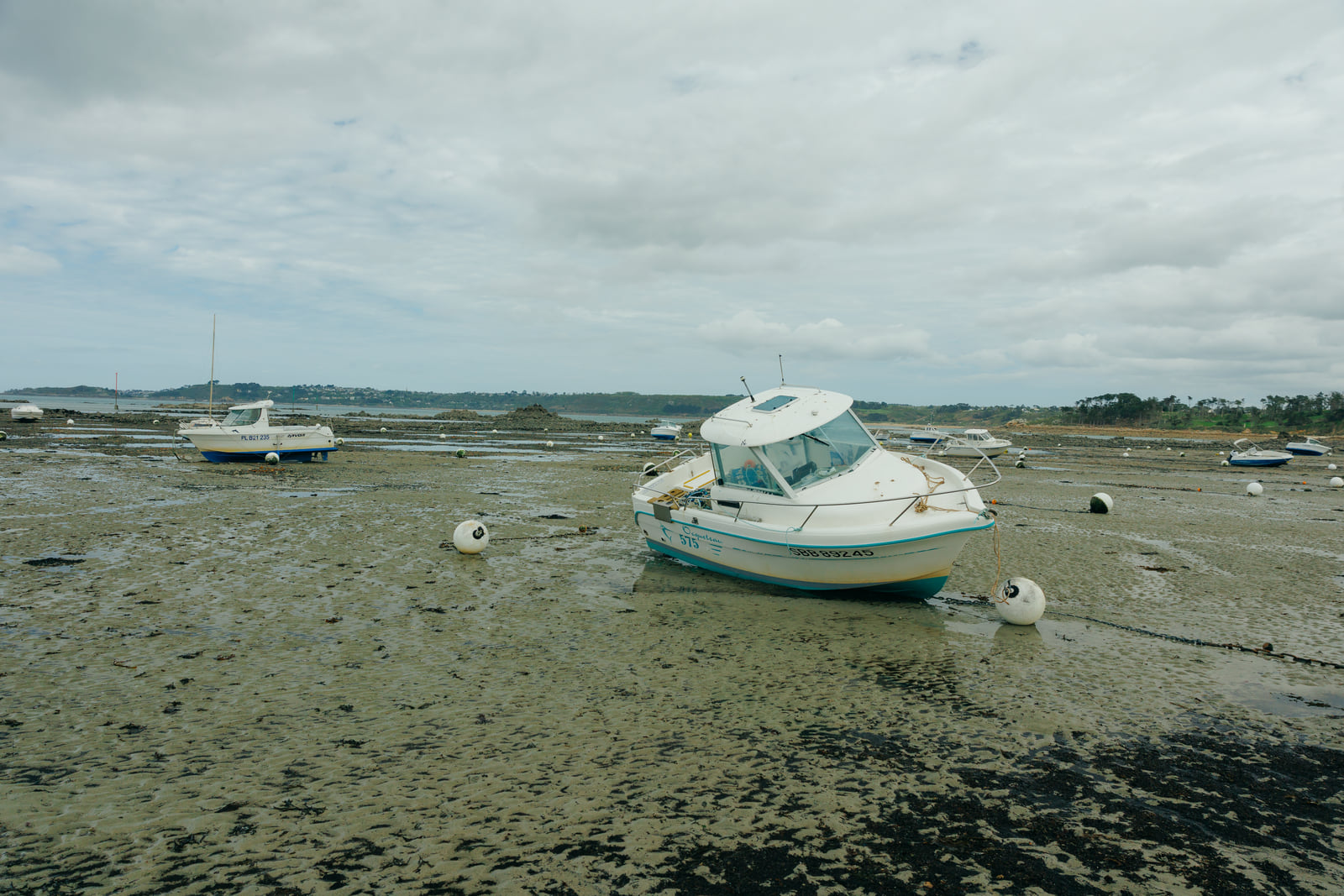 Boats stranded across a wide grey tidal flat.