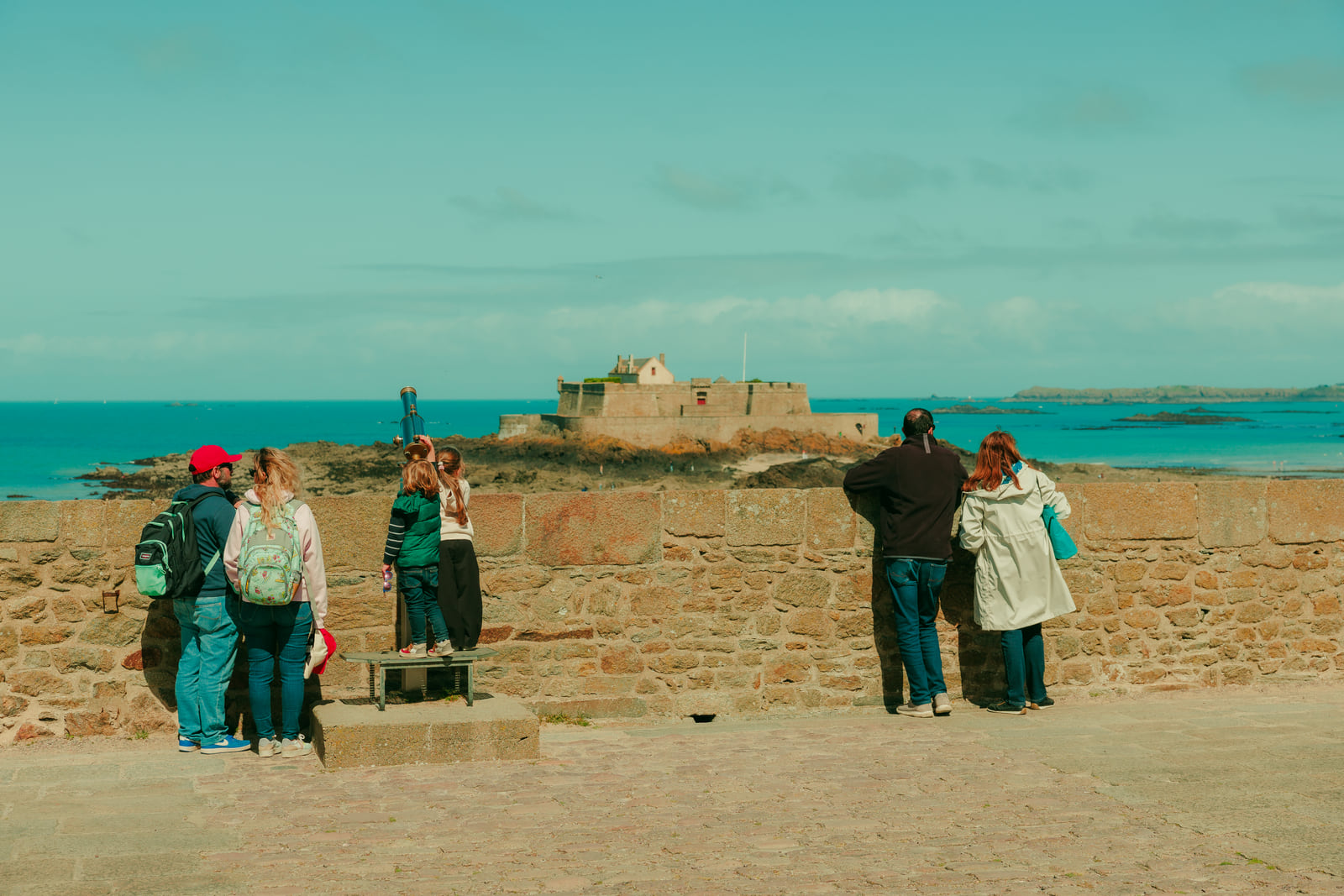 Small groups of people crossing a broad beach beneath a turquoise horizon.