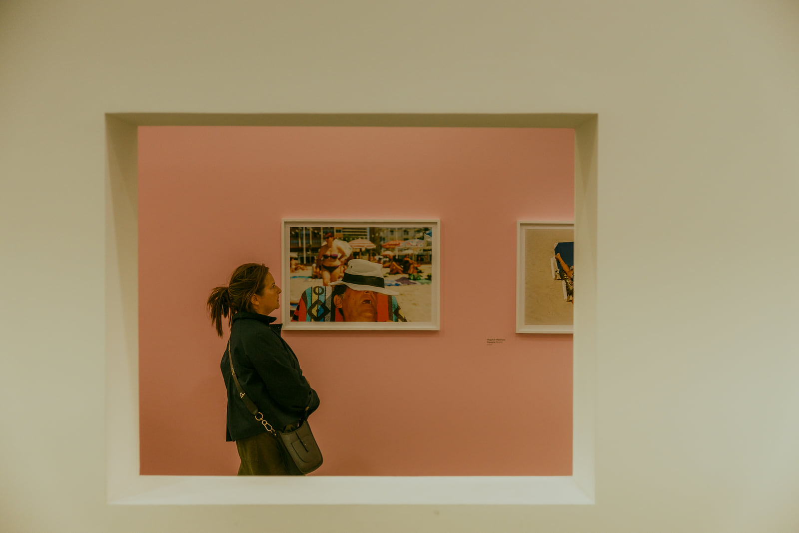 A visitor passing a small painting in a softly lit pink gallery.