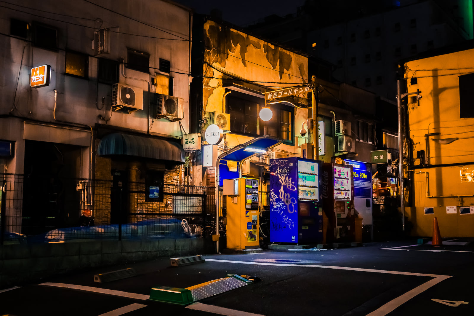 A blue-lit corner shop glowing on a quiet street at night.